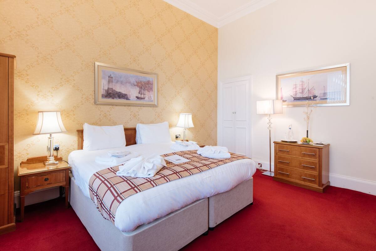 A hotel room with a large bed, two bedside tables with lamps, a wooden dresser, and two framed pictures on the walls.