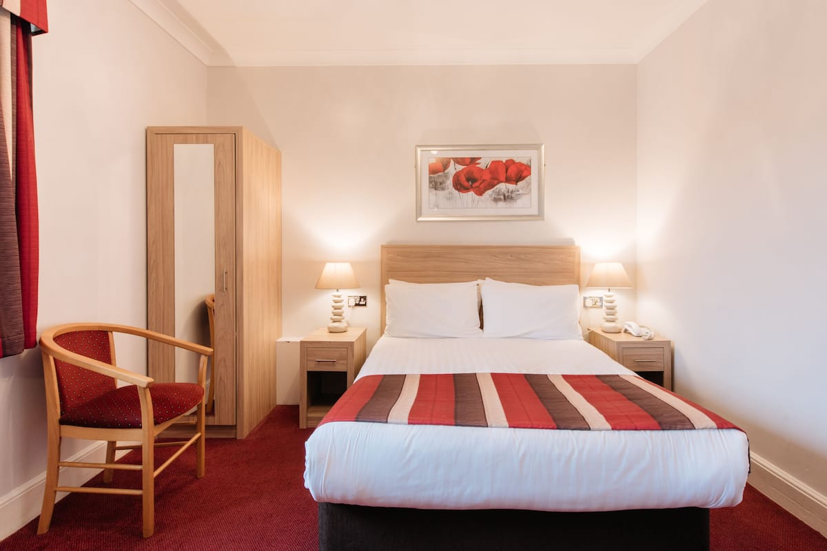 A hotel room with a bed, two bedside tables with lamps, a chair, a door, and a framed picture on the wall.