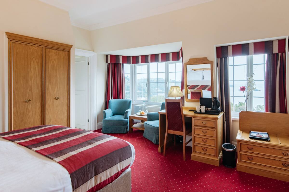 A hotel room with a bed, a desk, a chair, a wardrobe, and a window with curtains.