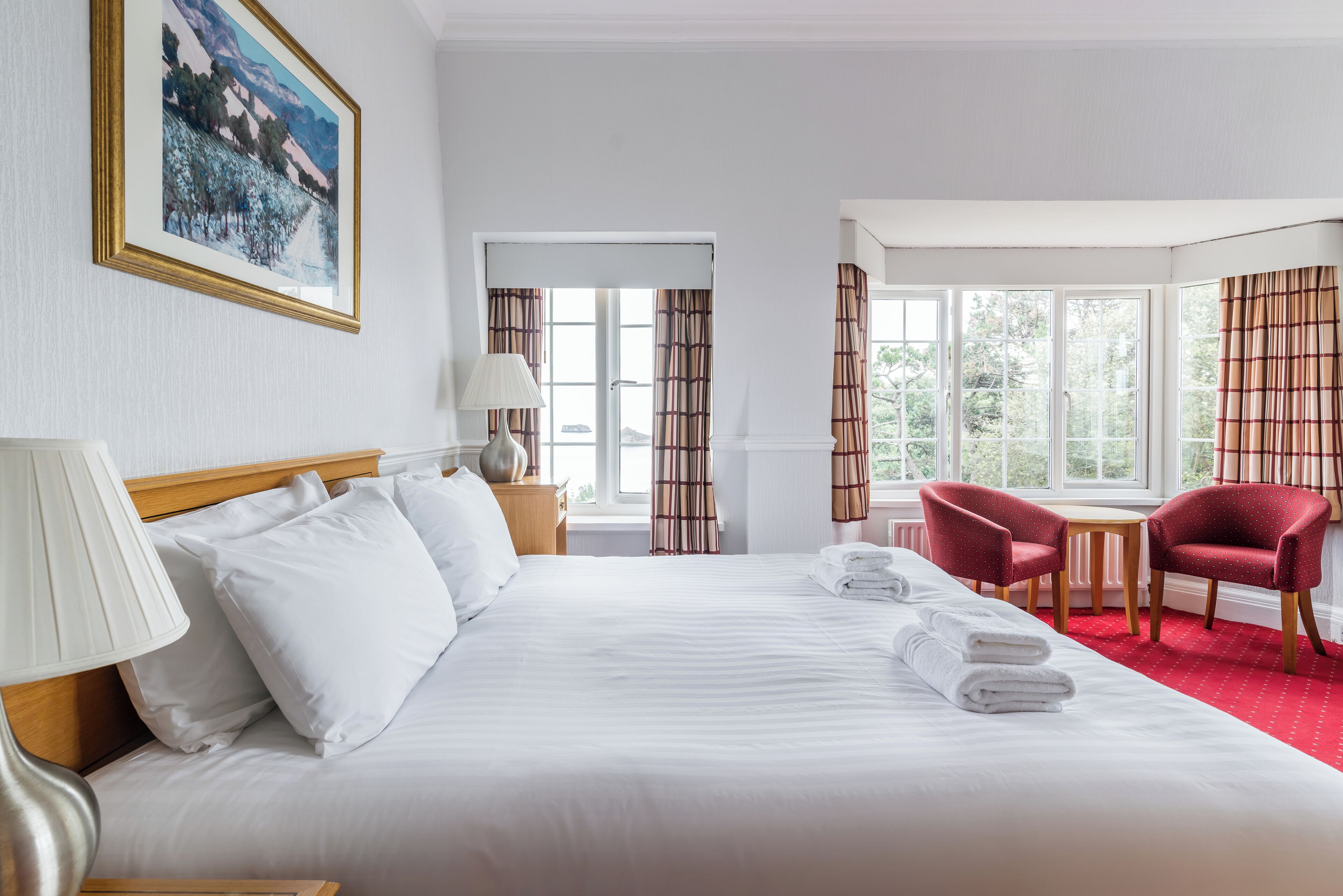 A hotel room with a large bed, a desk, two chairs, and a window with curtains.
