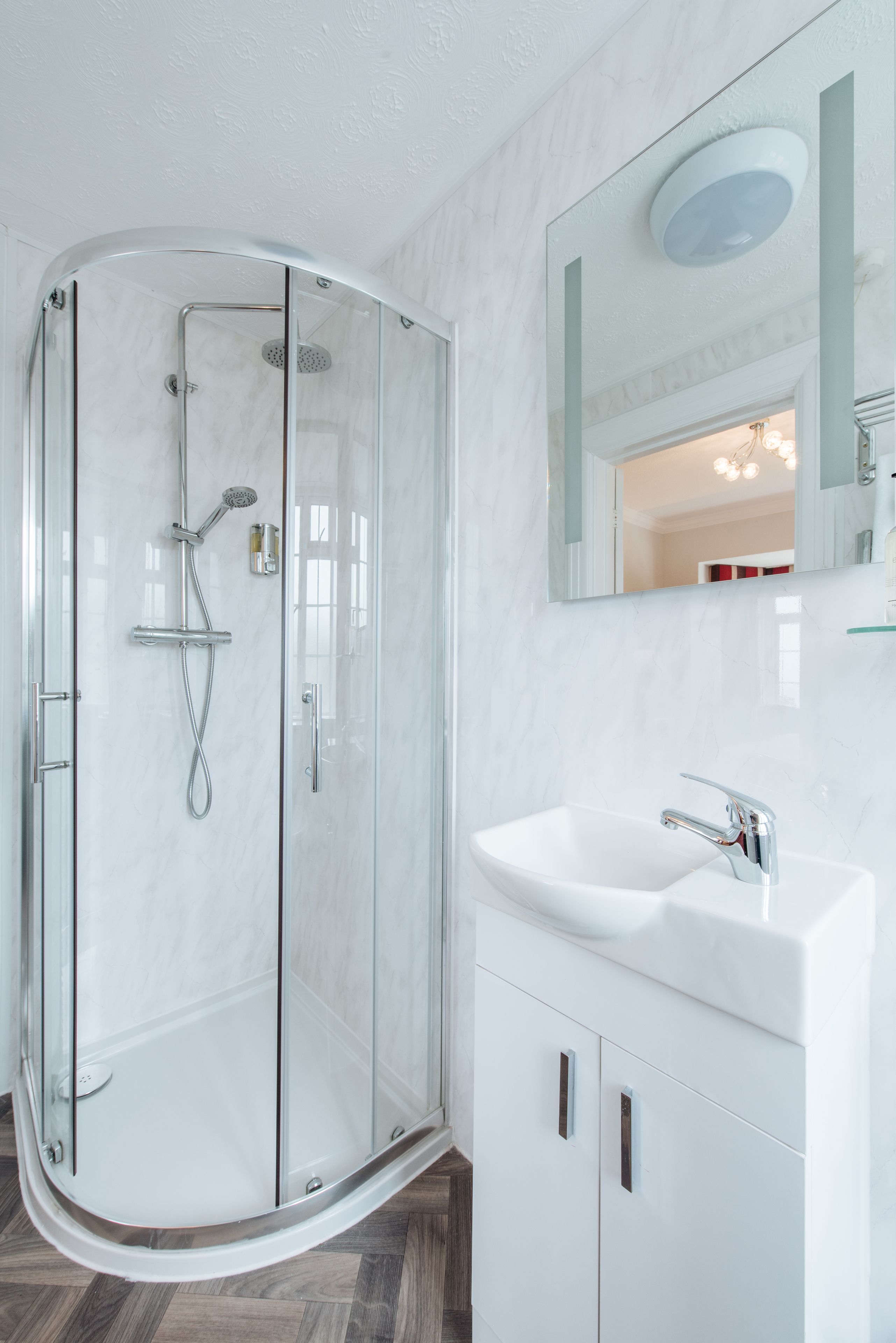 A modern bathroom with a glass-enclosed shower, a white sink, and a large mirror above the sink.