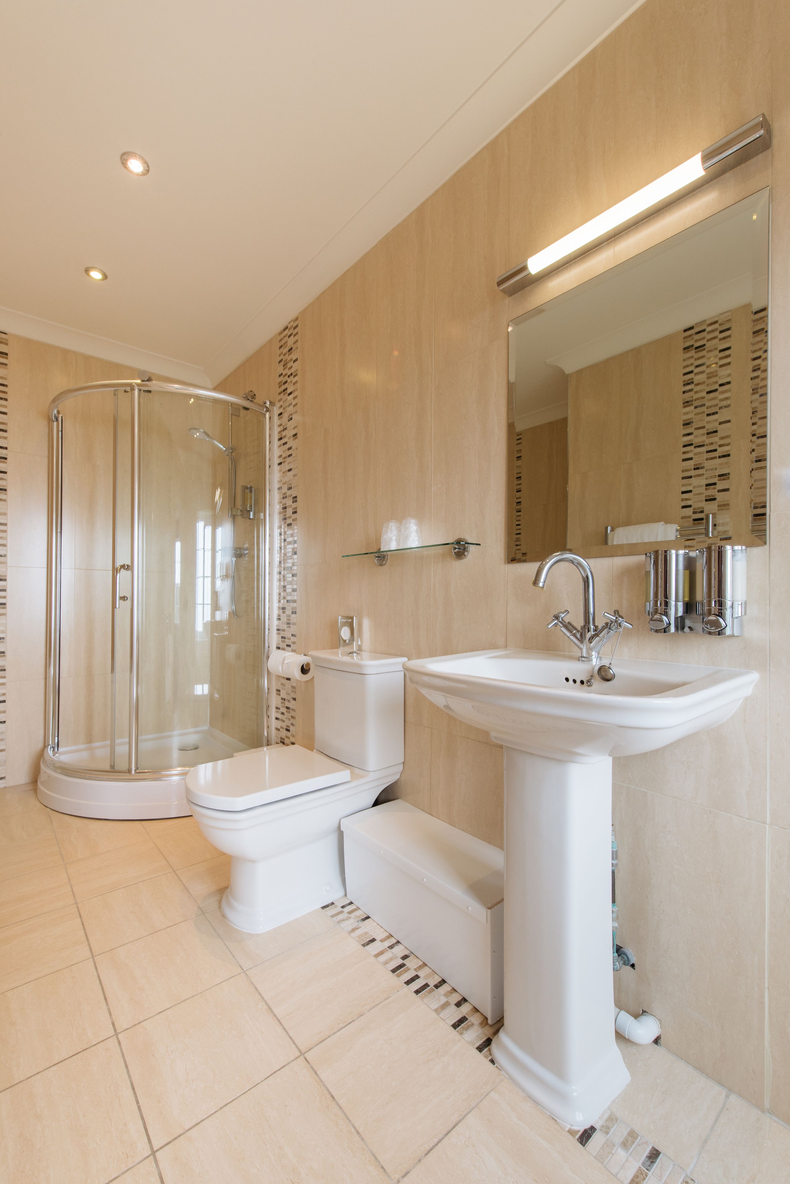 Een moderne badkamer met een douchecabine van glas, een wastafel op een voetstuk en een toilet.
