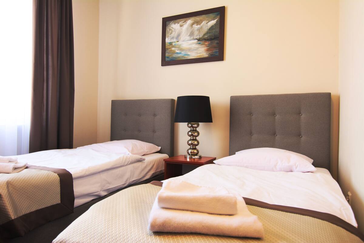 A hotel room with two beds, a painting on the wall, and a lamp on a nightstand.