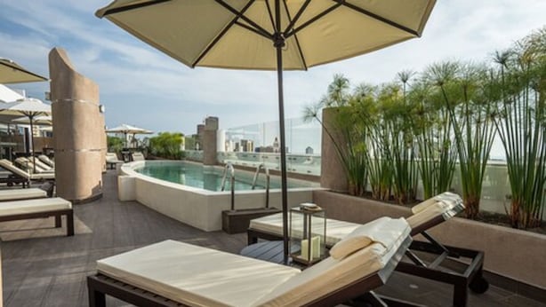 Un área de piscina en la azotea con sillones de descanso, un jacuzzi y sombrillas.