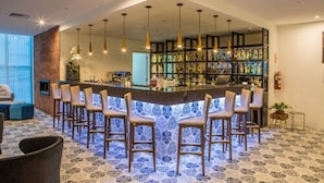Zona de bar con mostrador azulado de azulejos, múltiples lámparas colgantes y una variedad de botellas en estantes.