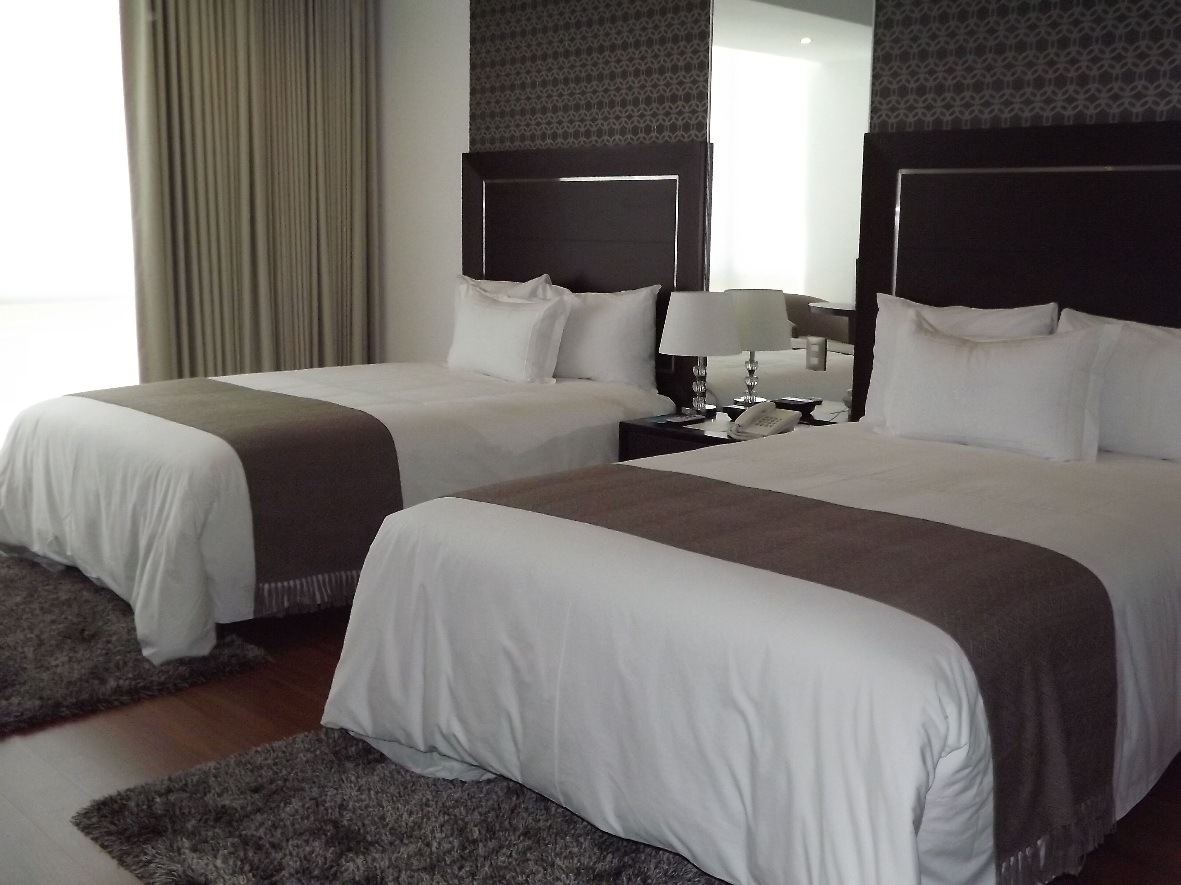 Una habitación de hotel con dos camas, una mesita de noche con lámpara y un espejo.