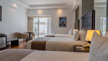 Une chambre d’hôtel avec deux lits, un bureau, une chaise, une lampe et une fenêtre donnant sur des immeubles.