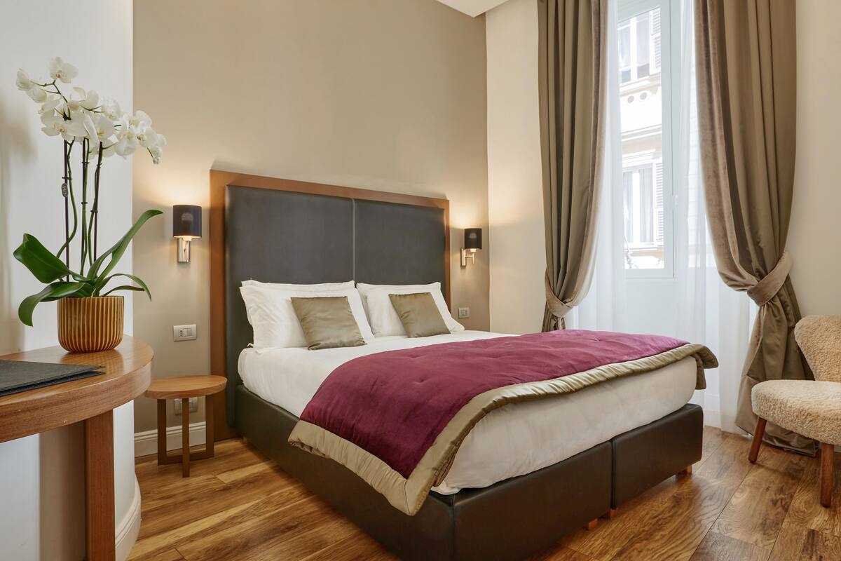 A modern bedroom with a bed, bedside tables, a potted plant, and a view of the outside.