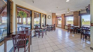 A spacious indoor area with multiple tables and chairs, large windows, and a clock on the wall. - Capital O Amerihost Inn and Suites Mexico Hwy 54 MO (Mexico)