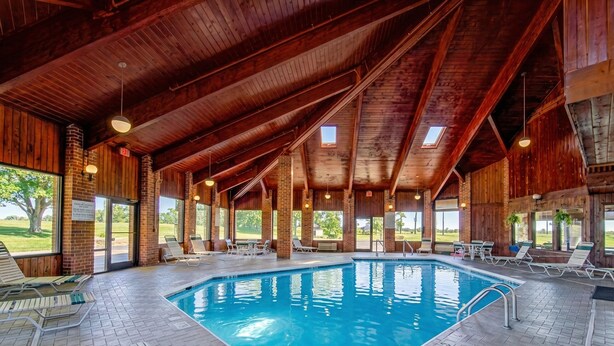 An indoor swimming pool with wooden beams, lounge chairs, and large windows. - Capital O Amerihost Inn and Suites Mexico Hwy 54 MO (Mexico)