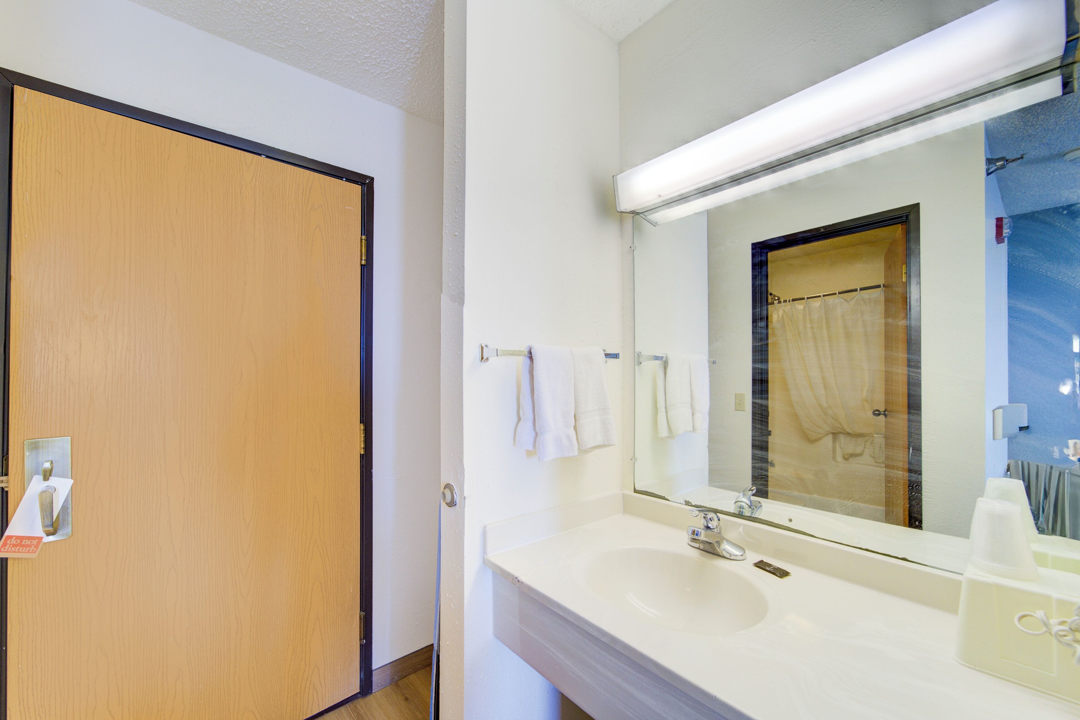 A bathroom with a wooden door, a white sink, a mirror, and a towel hanging on the wall.