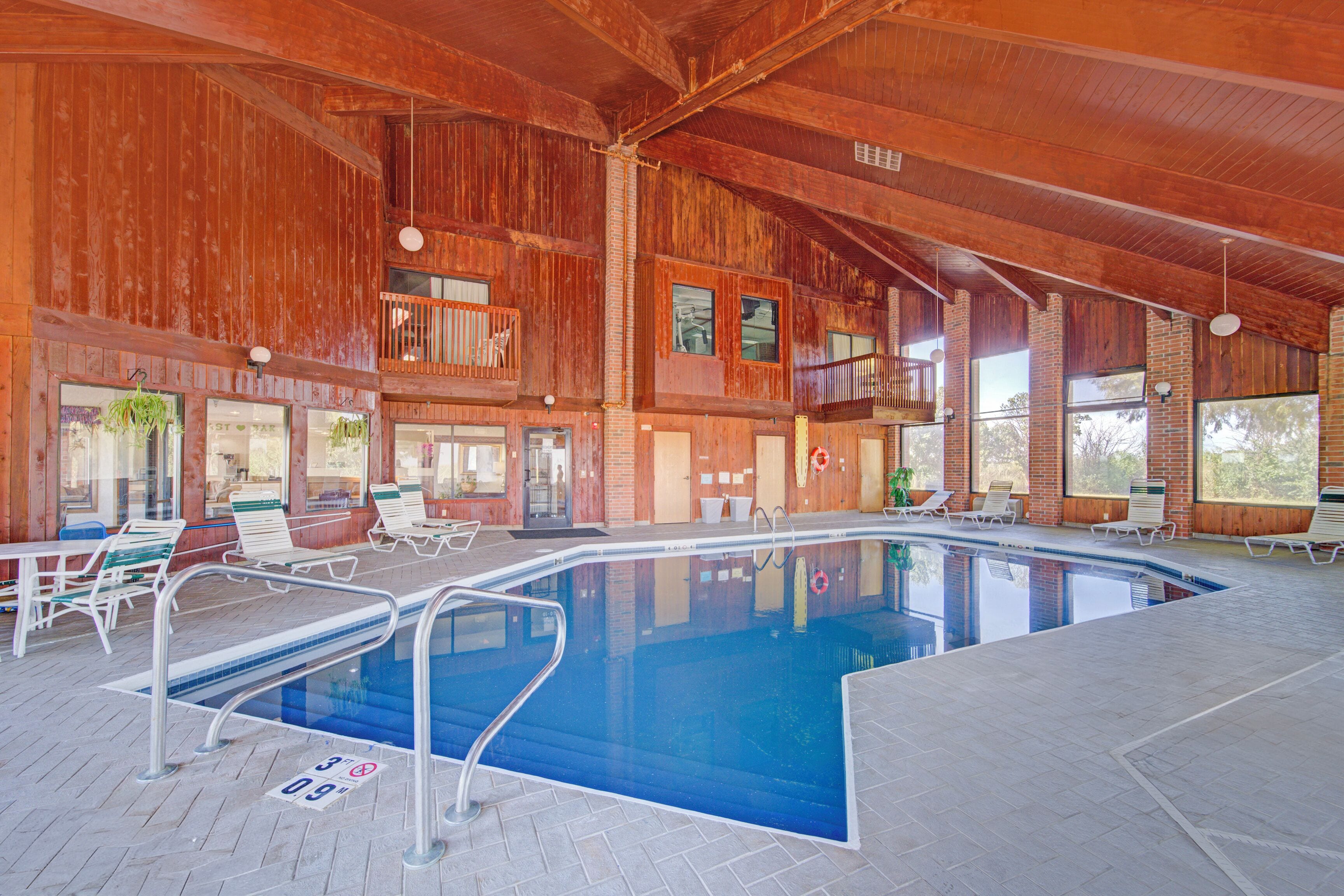An indoor swimming pool with a wooden interior, multiple lounge chairs, and a clear view of the sky through large windows.