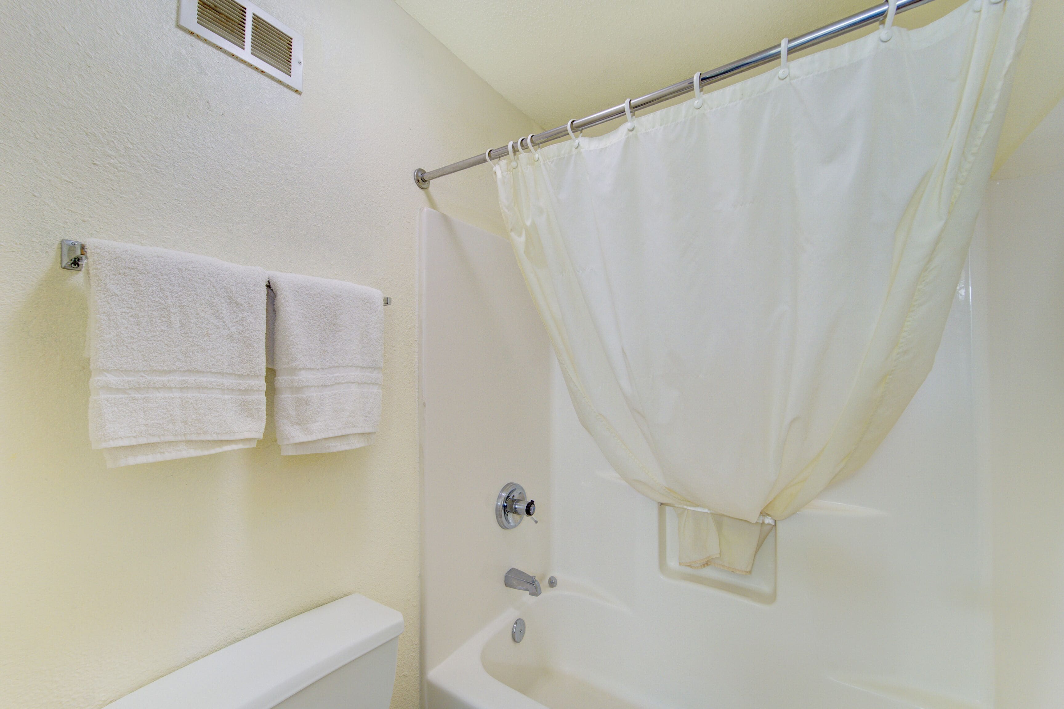 A bathroom with a bathtub, a shower curtain, and two towels hanging on the wall.