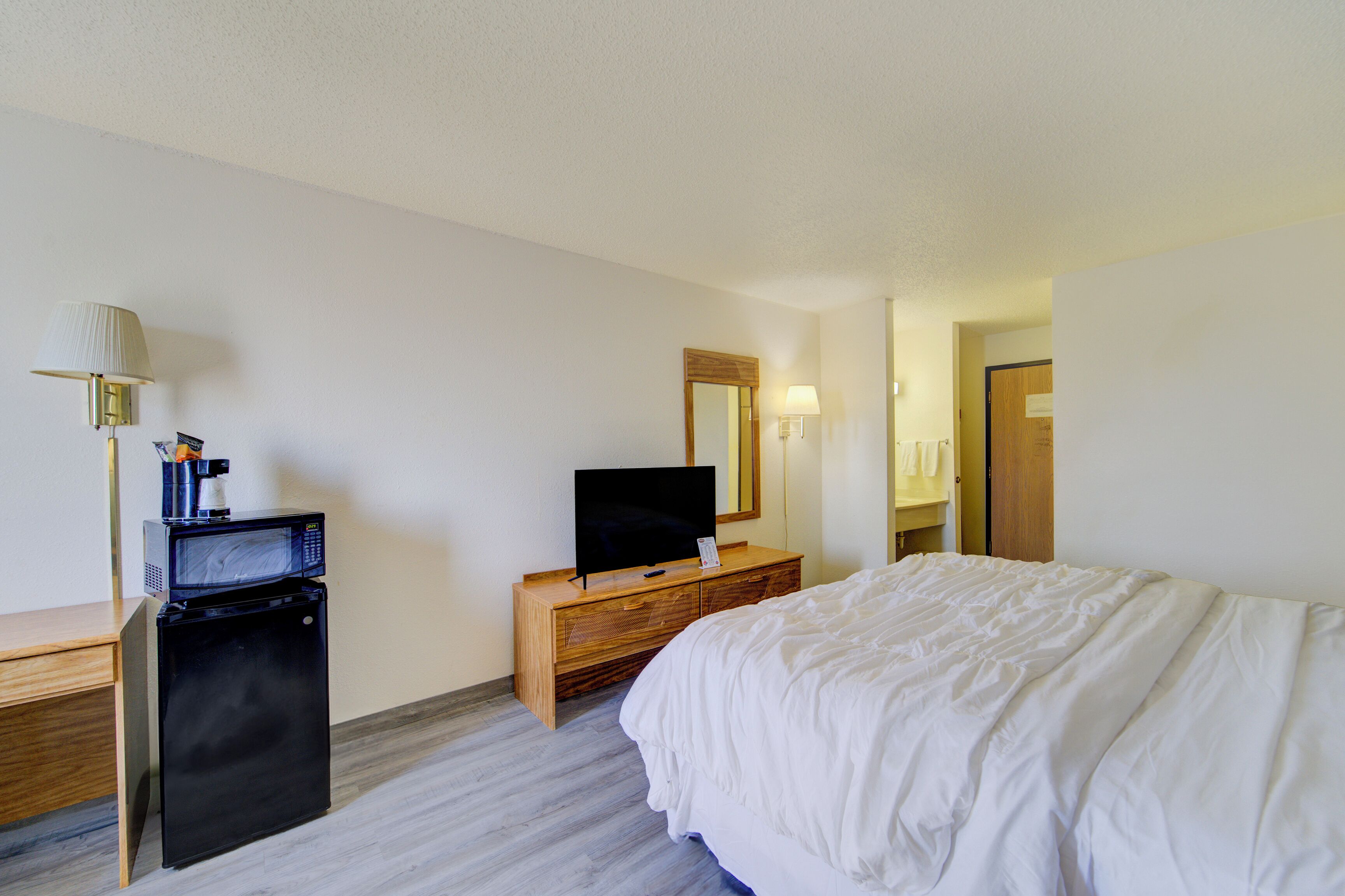 A hotel room with a bed, a television on a wooden dresser, a microwave, a lamp, and a mirror.