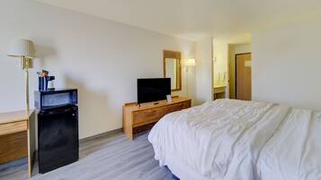 A hotel room with a bed, a television on a wooden dresser, a microwave, a lamp, and a mirror.