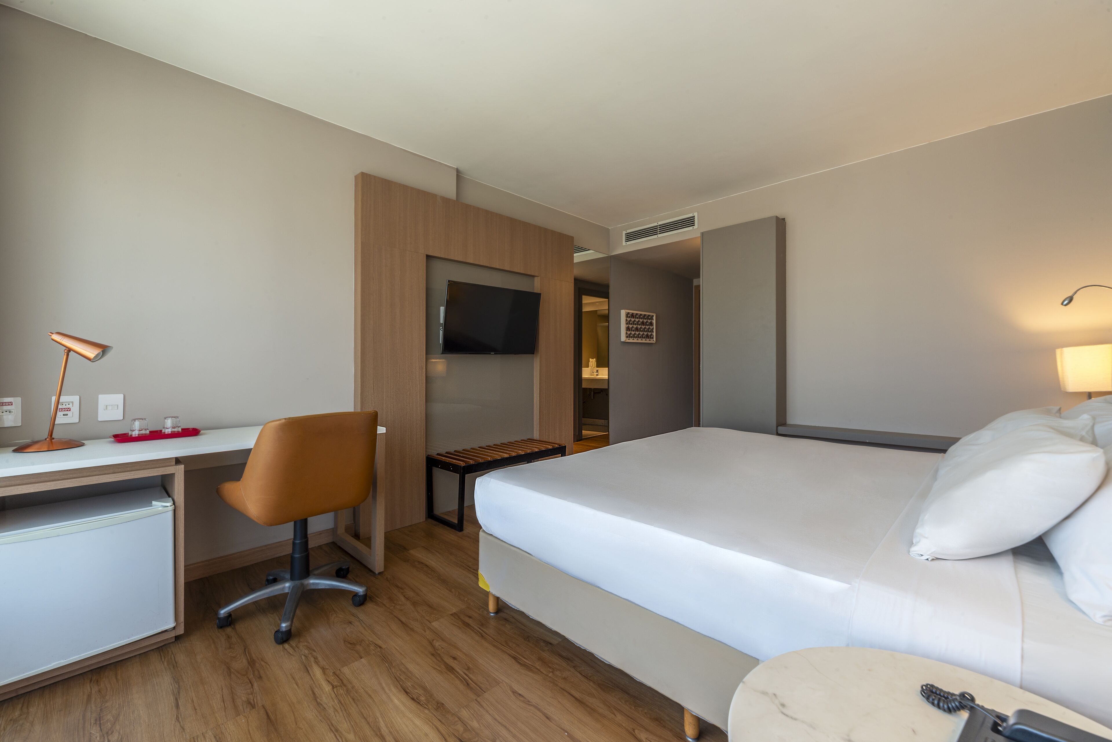 A hotel room with a bed, desk, chair, TV, and a small table.
