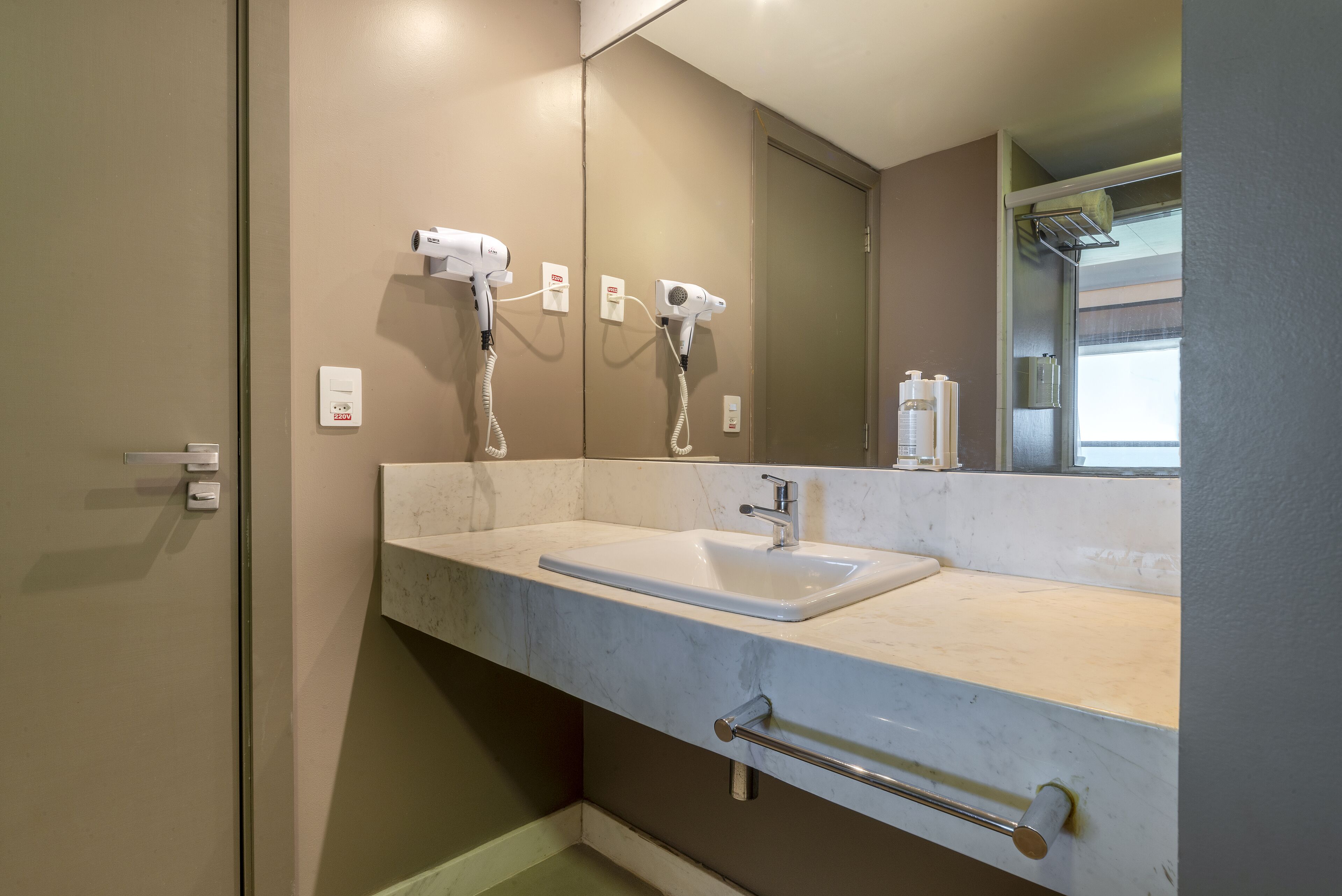A bathroom with a white sink, two hair dryers, a mirror, and a towel rack.