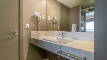 A bathroom with a white sink, two hair dryers, a mirror, and a towel rack.