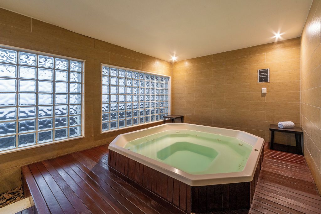 A spa room with a large freestanding bathtub, wooden flooring, and large windows with frosted glass panels.