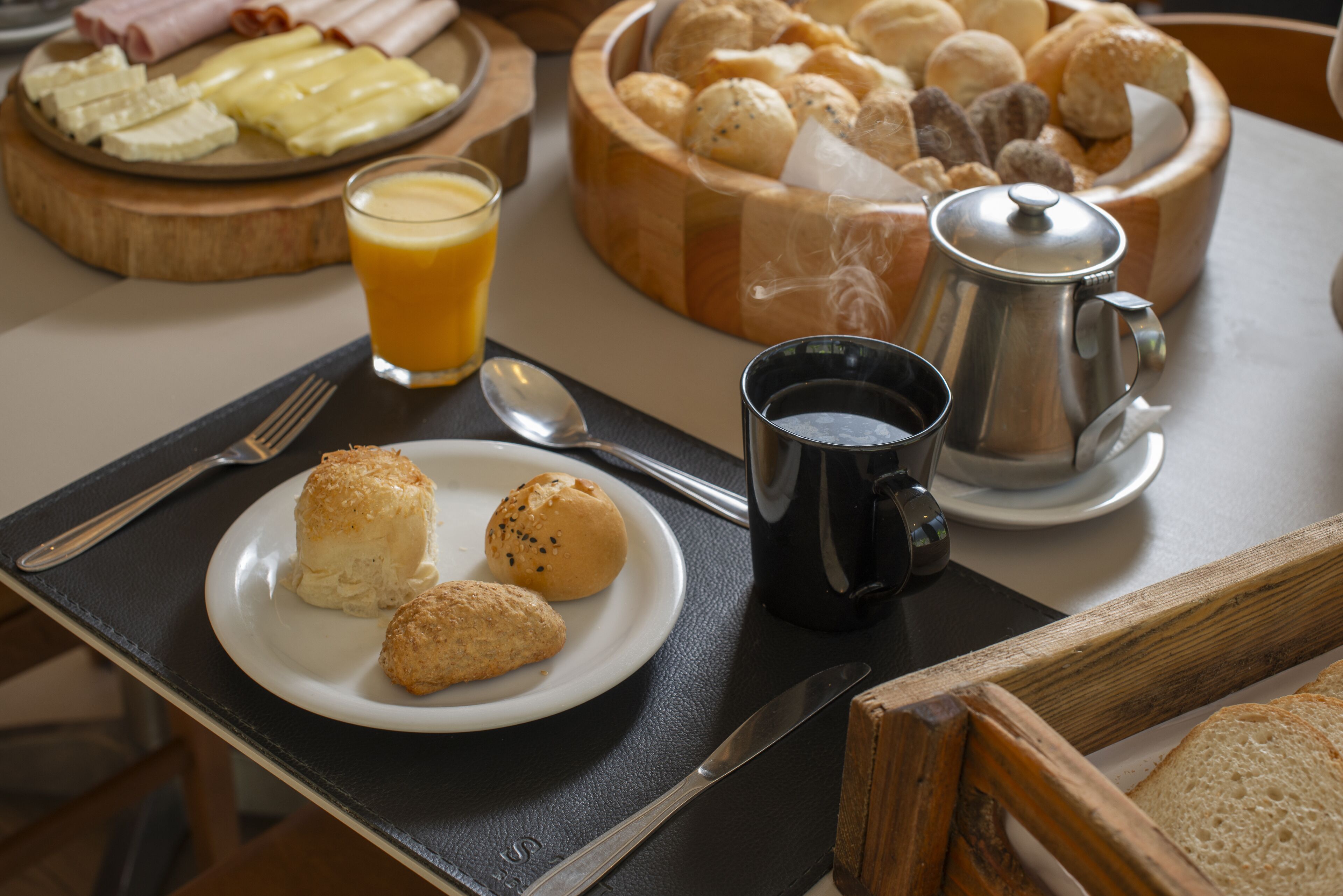 A breakfast setting with a plate of pastries, a coffee pot, and a glass of orange juice on a table.