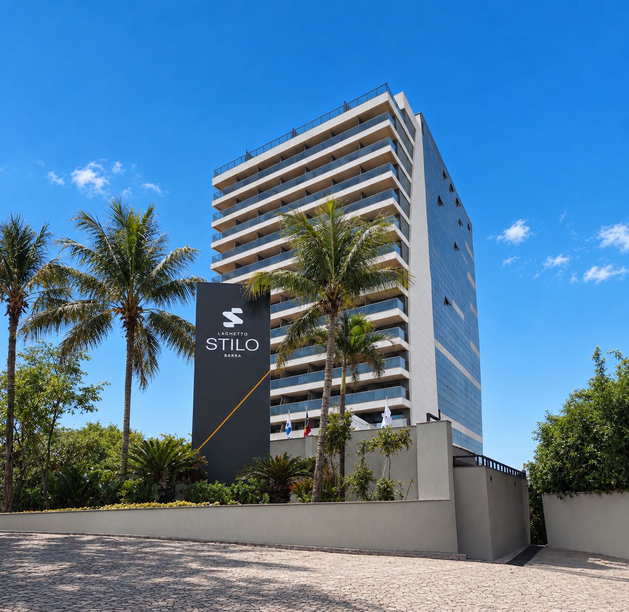 Ein modernes Hochhaus-Hotel mit einem auffälligen Schild für 'Stilo Barra' und einem strahlend blauen Himmel.