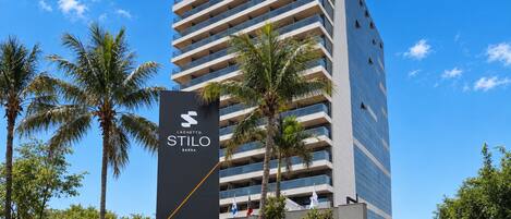 A modern high-rise hotel with a prominent sign for 'Stilo Barra' and a clear blue sky.