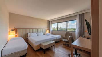 Habitación de hotel con dos camas, un escritorio, una silla y un ventanal con vistas a la ciudad.