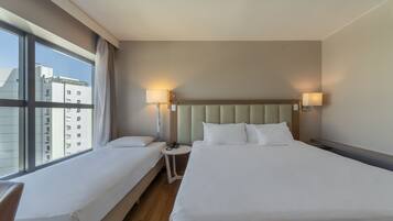 Habitación de hotel con dos camas, un ventanal grande y vistas a edificios.