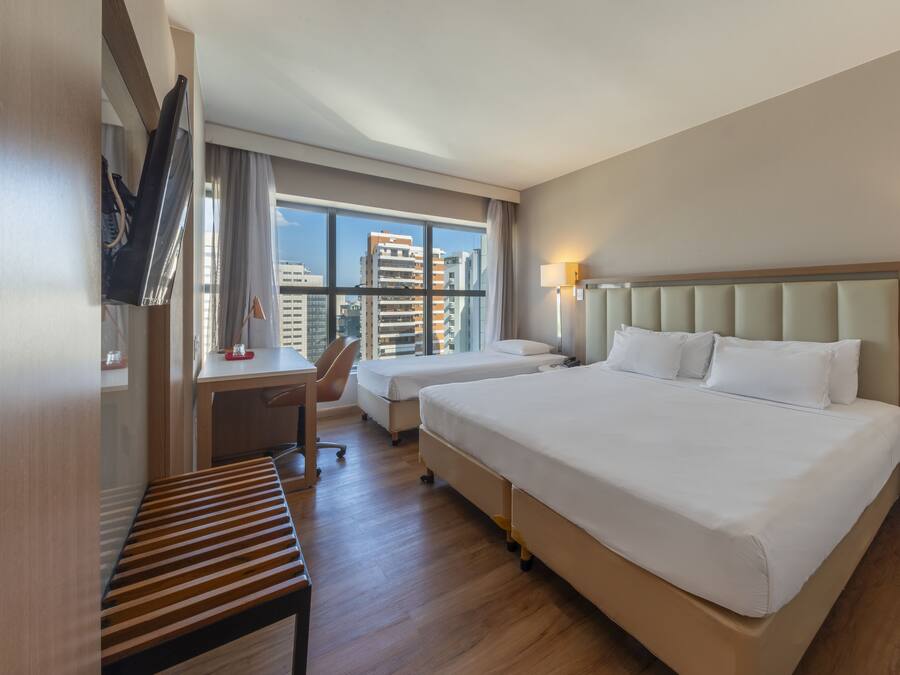 A hotel room with a large bed, a desk, a chair, and a view of the city.