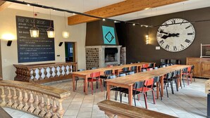 A restaurant with a long wooden table, chairs, a clock, and a menu on the wall. - Holiday Home in Somme-Leuze with Garden BBQ (Noiseux)