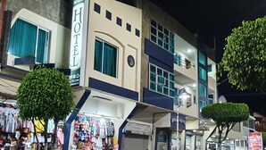 A hotel with a sign indicating it is a Meraki hotel, featuring a ground floor with shops and a visible staircase leading to the upper floors.
