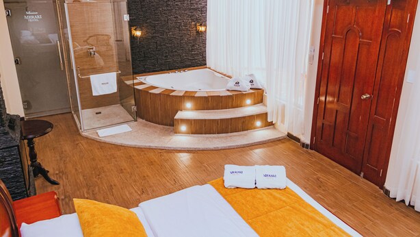 A hotel room with a wooden floor, a glass-enclosed shower, a wooden bathtub, and a wooden door.