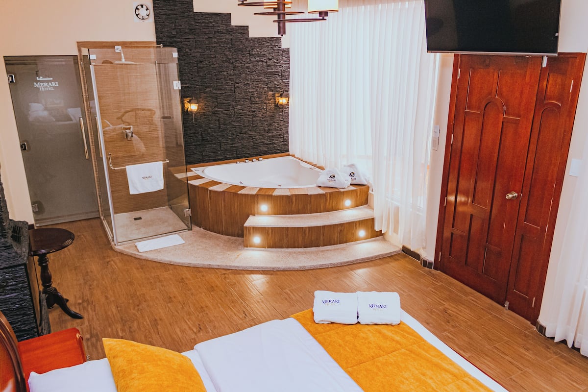 A hotel room with a wooden floor, a glass-enclosed shower, a wooden bathtub, and a wooden door.