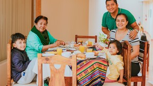 A family dining at a wooden table with chairs, a colorful tablecloth, and various breakfast items.