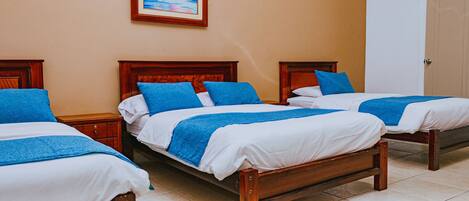 A hotel room with three wooden beds, each with blue and white bedding.