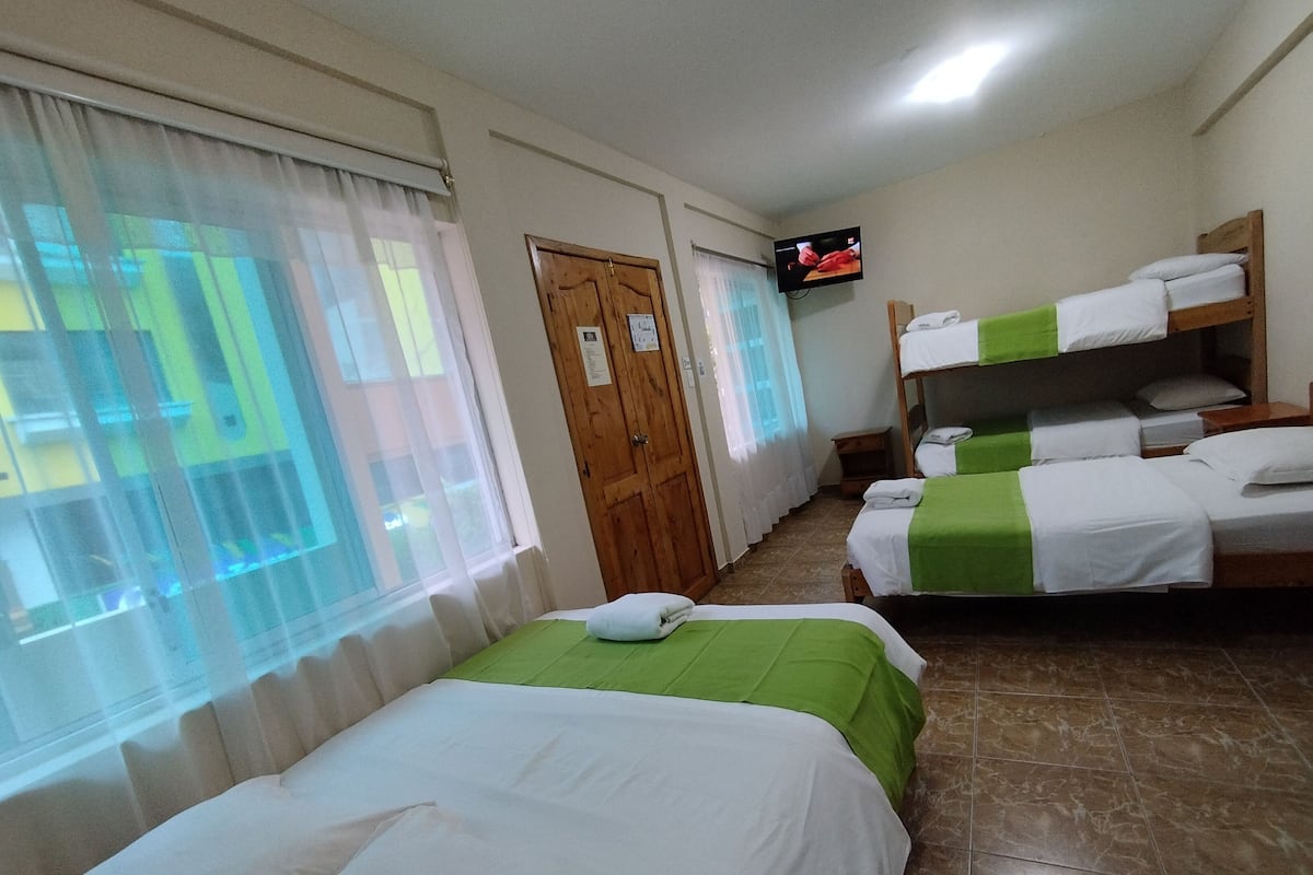 A hotel room with two single beds, a TV mounted on the wall, and a wooden door.