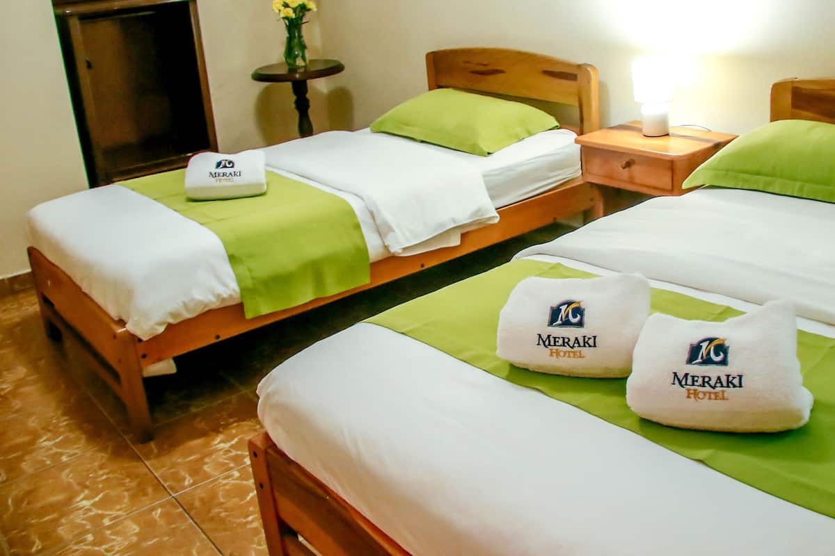 A hotel room with two beds, each with a green pillow and a white blanket. There is a nightstand with a lamp and a vase with flowers.