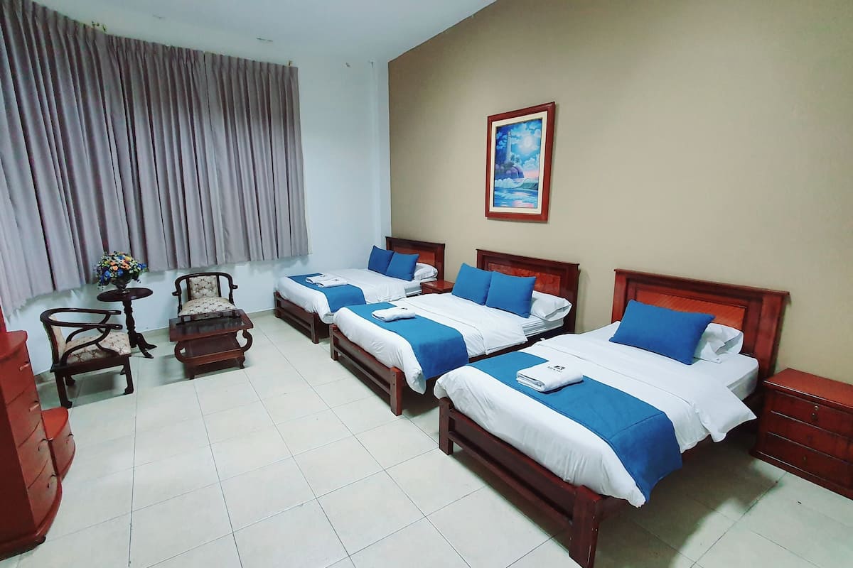 A hotel room with two beds, a small table with a vase, a chair, and a wooden cabinet.