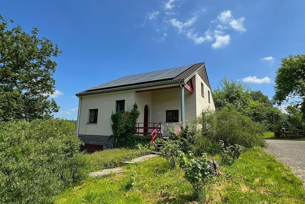 Un petit bâtiment d’un seul étage, doté d’un toit en pente, entouré de verdure et surplombé d’un ciel bleu clair.