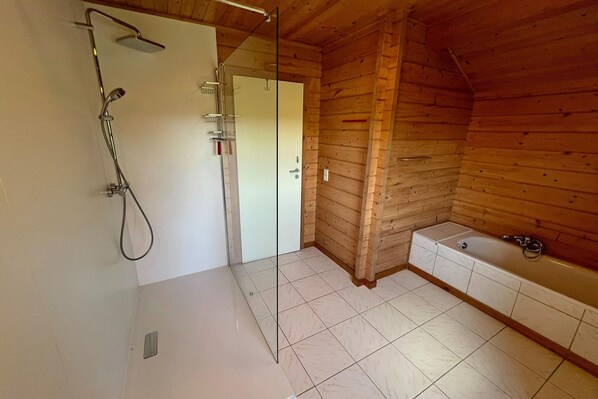 A modern bathroom with a glass shower enclosure, a bathtub, and wooden walls.