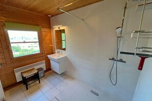Une salle de bain avec un plafond en bois, une fenêtre donnant sur un beau paysage, un lavabo blanc, un miroir et une douche.