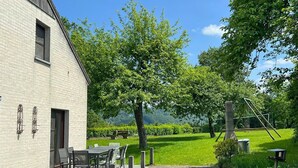 A building with a brick exterior, a patio with a table and chairs, and a grassy area with trees and a playground. - Chalet in Hampteau with Valley Views (Hampteau)