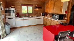 A compact kitchen with wooden cabinets, a stainless steel oven, a microwave, and a red dining table. - Chalet in Hampteau with Valley Views (Hampteau)