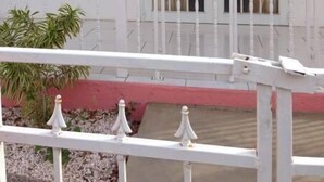 Un bâtiment blanc avec une grande fenêtre et une porte, un petit balcon avec une balustrade et un pot de fleurs.