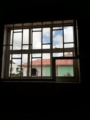 A window with a grid pattern, through which a building with a red roof and green walls is visible. - Curacao Vacation Homes (Willemstad)