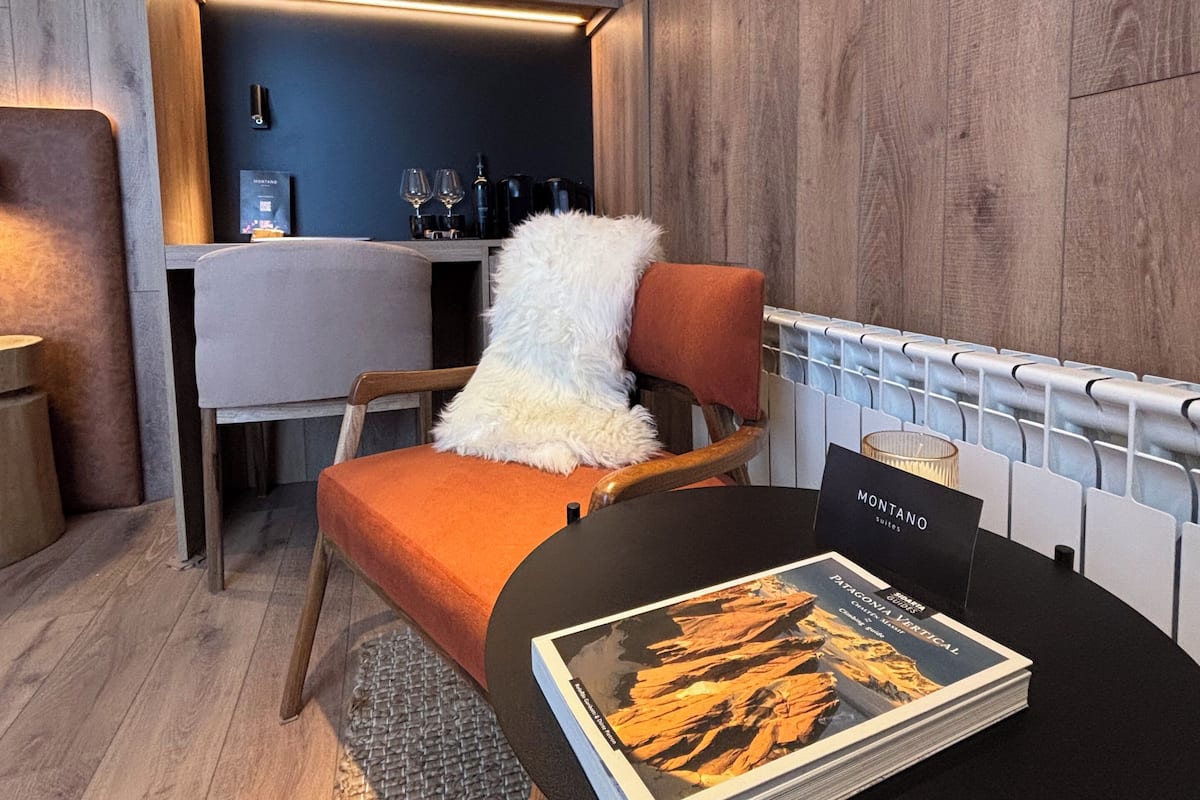 A modern room with a wooden floor, a sofa with a fluffy white throw, a table with a magazine, and a bar area with glasses and bottles.