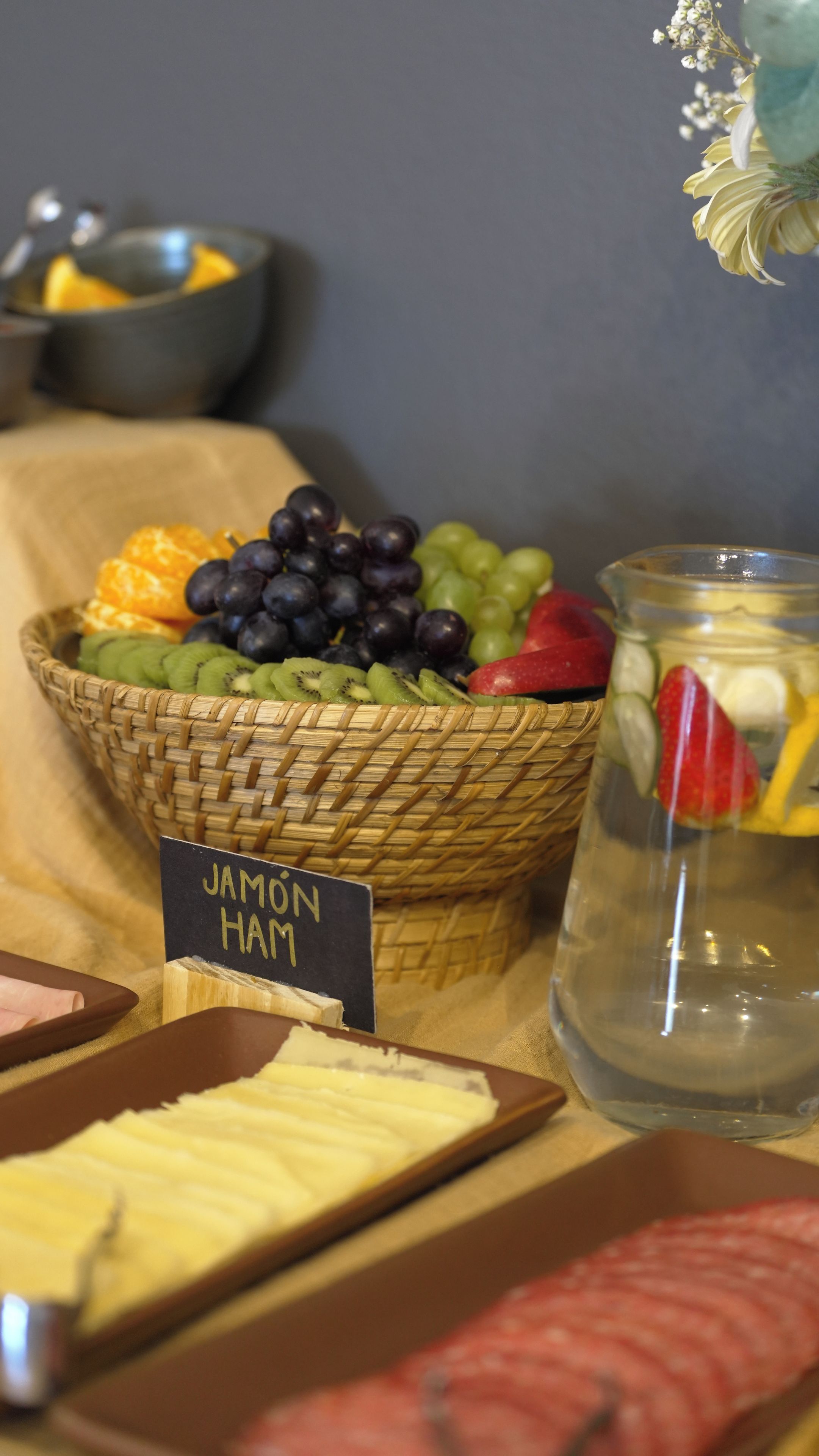 A fruit basket with a label, a jar of jam, and a sign indicating 'JAMON HAM'.
