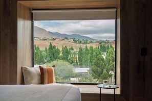 A bedroom with a large window offering a view of a town and mountains.