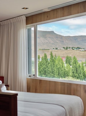 A hotel room with a large window offering a view of a mountainous landscape and a small town.
