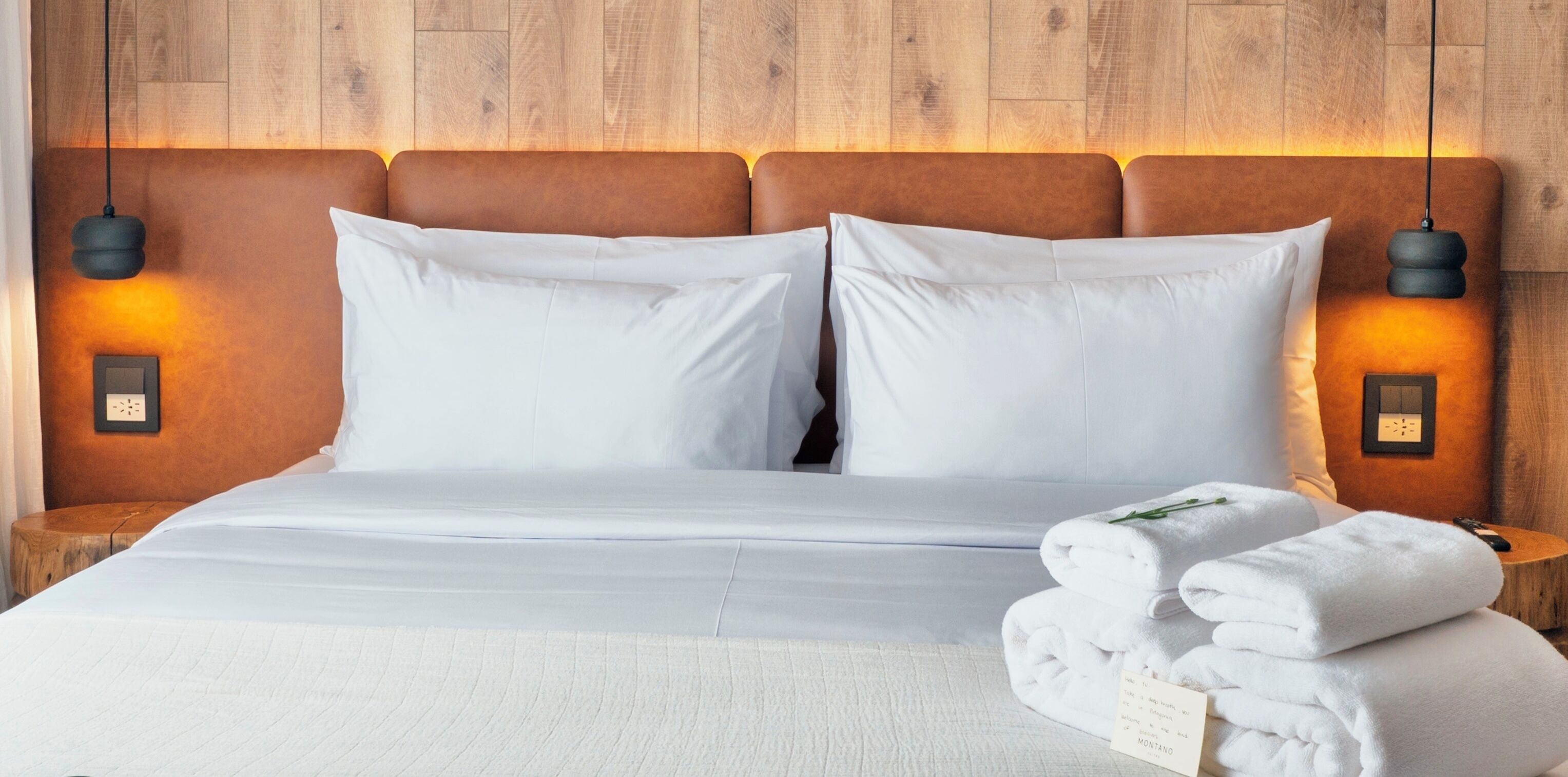 A neatly made bed with white linens, two pillows, and a stack of folded towels on the side.
